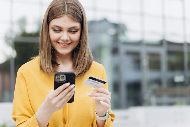 Glimlachend meisje met creditcard en smartphone zittend op bankje stadsgebouwen buiten gelukkige vrouw