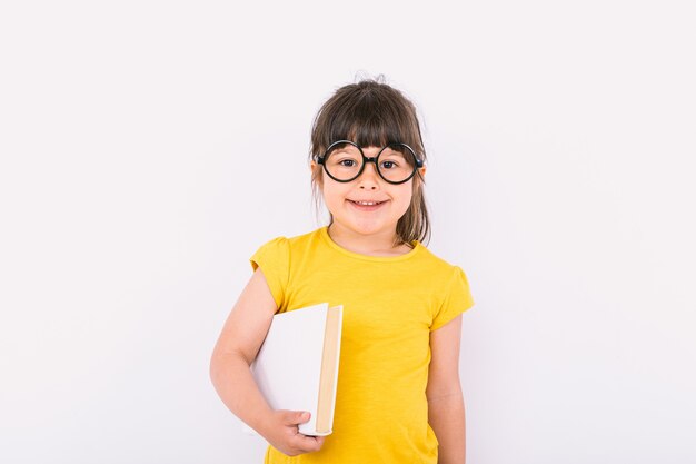 Glimlachend meisje met een geel t-shirt en een ronde zwarte bril met een boek in haar handen op een witte achtergrond