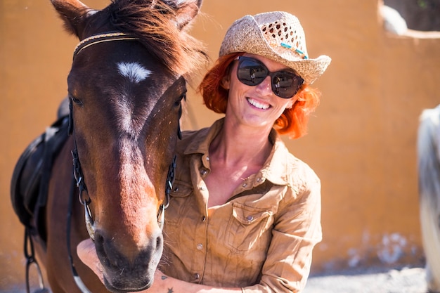 Glimlachend meisje met rood haar en cowboyhoed poseren met haar paard.