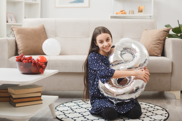 Glimlachend meisje op gelukkige vrouwendag zittend op de vloer met nummer acht ballon in de woonkamer