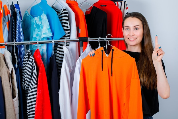Glimlachend meisje toont een klein gebaar door sweetshirt op kledingachtergrond te houden