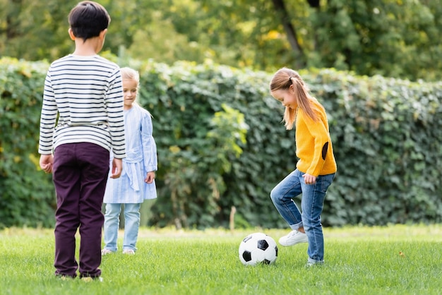 Glimlachend meisje voetballen in de buurt van vrienden op grasveld