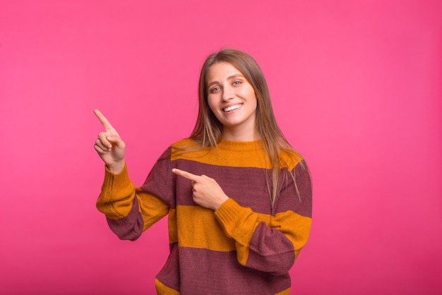 Glimlachend meisje wijst met beide handen op de roze achtergrond.