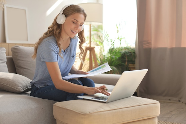 Glimlachend meisje zit in de buurt van bank kijken naar webinar op laptop. gelukkige jonge vrouwenstudie op online verre cursus.