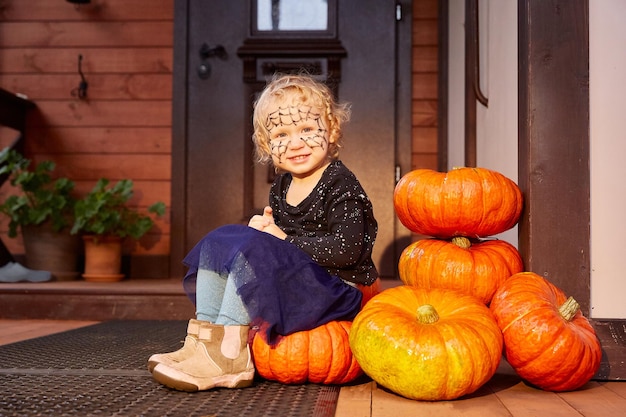 Foto glimlachend meisje zit naast pompoenen bij de deur van het huis halloween decor