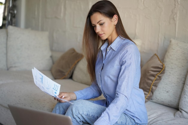 Glimlachend meisje zit op de bank en kijkt naar webinar op laptop Gelukkige jonge vrouw studeert online cursus op afstand