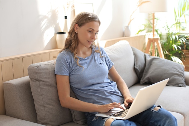 Glimlachend meisje zit op de bank en kijkt naar webinar op laptop. Gelukkige jonge vrouwenstudie op online verre cursus.