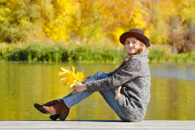 Glimlachend meisje zittend op de pier met herfstbladeren in handen zonnige dag