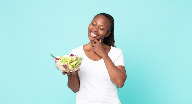 Glimlachend met een gelukkige, zelfverzekerde uitdrukking met de hand op de kin en een salade in de hand