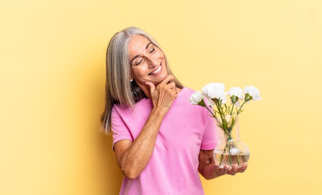 Glimlachend met een gelukkige, zelfverzekerde uitdrukking met de hand op de kin, verwonderd en opzij kijkend met decoratieve bloemen