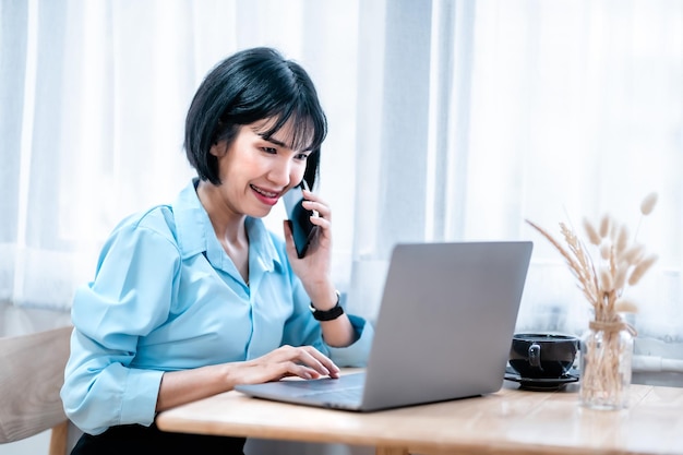 Glimlachend met tandheelkundige accolades Aziatische freelance mensen zakelijke vrouw houden smartphone oppakken casual werken met laptopcomputer met koffiekopje en smartphone in coffeeshop zoals de achtergrond