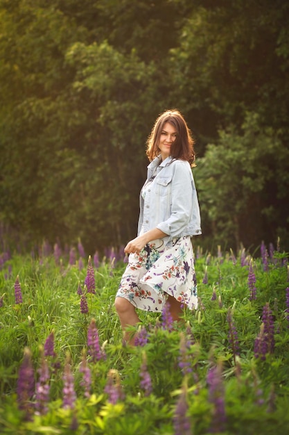 Foto glimlachend modieus brunette meisje in een veld met paarse lupinen