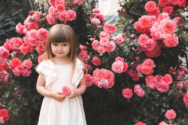 Glimlachend mooi schattig meisje van 45 jaar oud houdt roze roze bloem vast boven bloeiende struik in de tuin