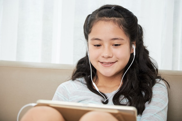 Glimlachend mooi tienermeisje met oordopjes bij het kijken naar een show op tabletcomputer