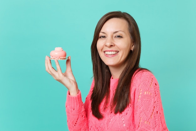 Glimlachend mooie jonge vrouw in gebreide roze trui met in de hand taart geïsoleerd op blauwe turquoise muur achtergrond, studio portret. Mensen oprechte emoties, lifestyle concept. Bespotten kopie ruimte.