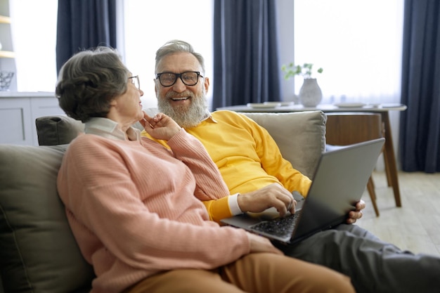 Glimlachend oudere echtpaar kijkt naar elkaar terwijl ze een laptop gebruiken