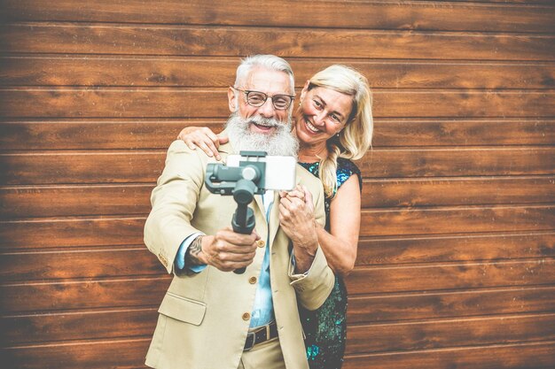 Foto glimlachend oudere echtpaar neemt een selfie met een mobiele telefoon terwijl ze tegen een houten muur staan