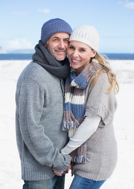 Glimlachend paar dat zich op het strand in warme kleding bevindt