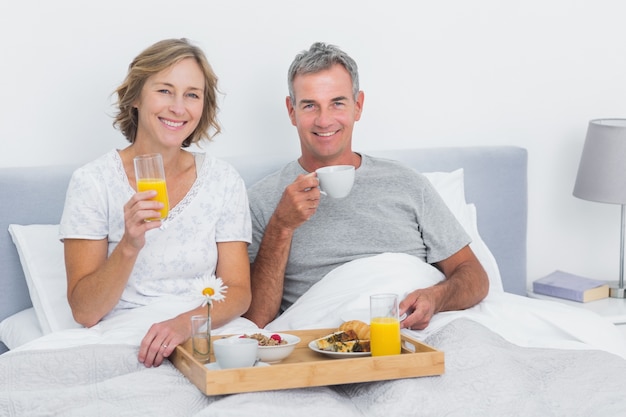 Glimlachend paar die ontbijt in bed hebben samen