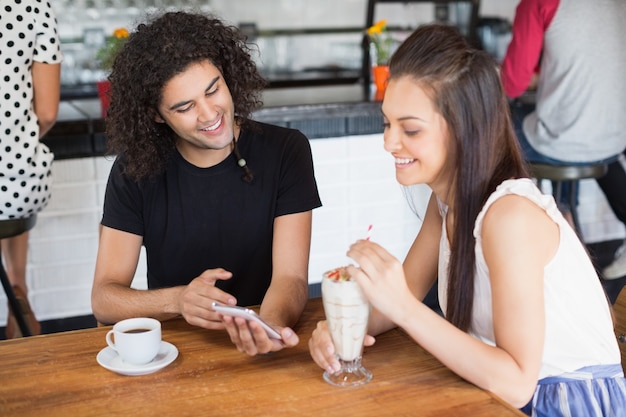 Glimlachend paar met behulp van mobiele telefoon terwijl het hebben van drankjes in restaurant