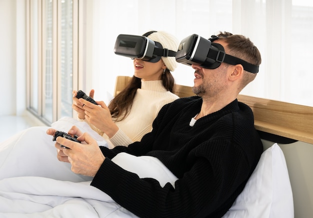 Glimlachend paar met VR-bril en het spelen van videogames met controller in bed. Gaming en technologie concept