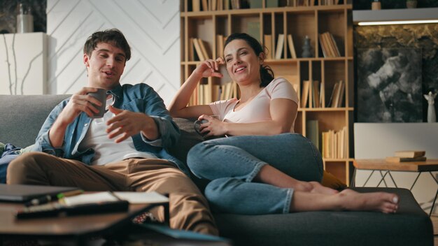 Glimlachend paar praat op de bank met kopjes koffie koppel ontspannende familie avond