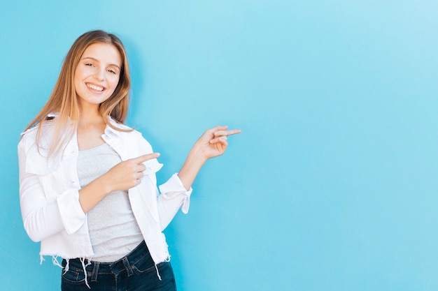 Glimlachend portret van een jonge vrouw die haar vinger richt tegen blauwe achtergrond