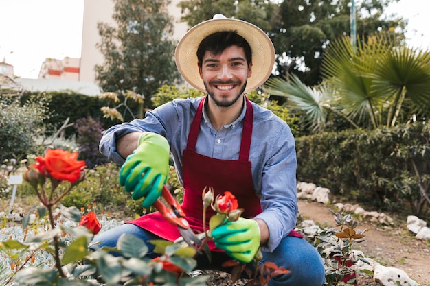 Glimlachend portret van een mannelijke tuinman die de roze bloem snoeit met snoeischaar