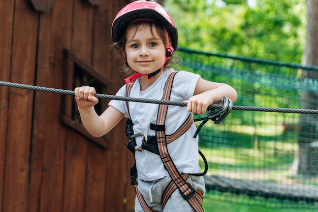 Glimlachend, positief meisje leunde op een touw aan het einde van de kabelbaan. Mooie baby bij het voltooien van obstakels