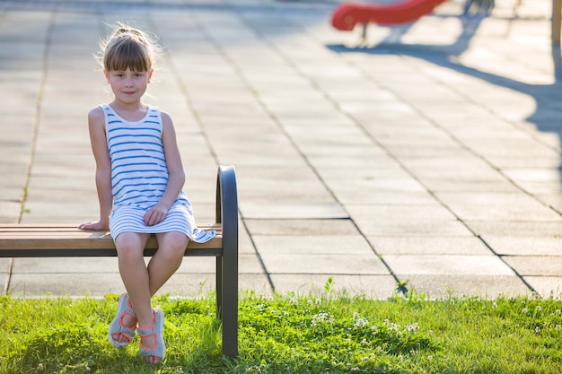 Glimlachend schattig jong meisje zit alleen buitenshuis op een bankje