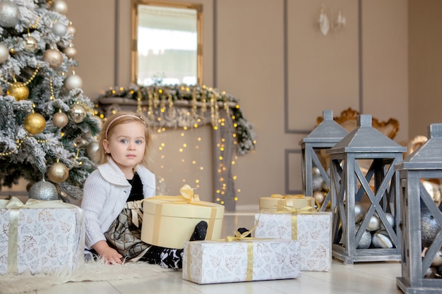 Glimlachend schattig klein meisje het openen van een kerstcadeau, de achtergrond kerstboom