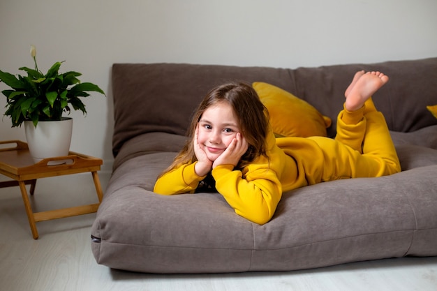 Glimlachend schattig klein meisje in gele kleren liggend in bed met een koptelefoon op het luisteren naar de muziek