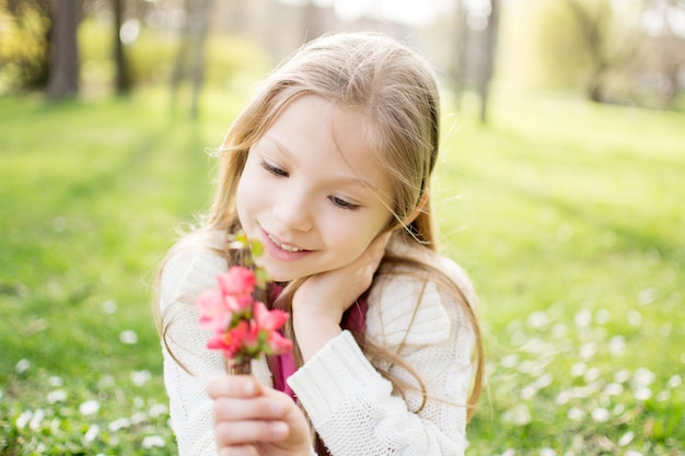 Glimlachend schattig klein meisje op de weide in het voorjaar bloem te houden en naar hem te kijken.