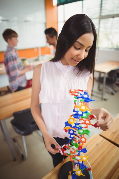 Glimlachend schoolmeisje dat het molecuulmodel in laboratorium onderzoekt