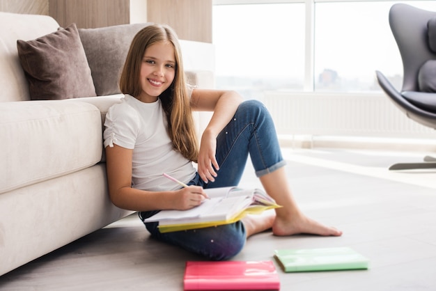 Foto glimlachend schoolmeisje zit op de vloer met notitieboekjes