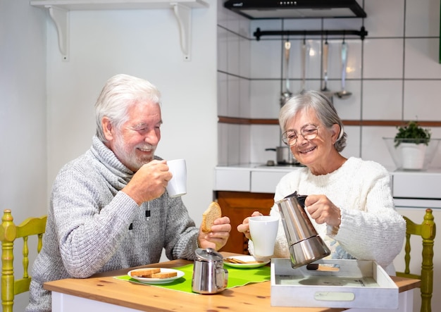 Glimlachend senior paar ontbijten samen aan tafel thuis vrouw met een koffiezetapparaat
