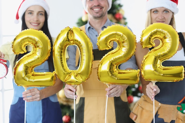 Glimlachend team van geüniformeerde werknemers houdt nummers tegen de achtergrond van nieuwjaarsboom Kerstmis