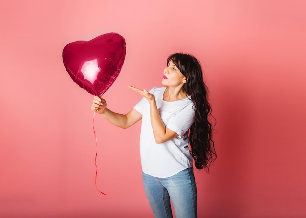 Glimlachend tevreden blank meisje poserend met een rode hartvormige ballon op een roze achtergrond Valentijnsdag