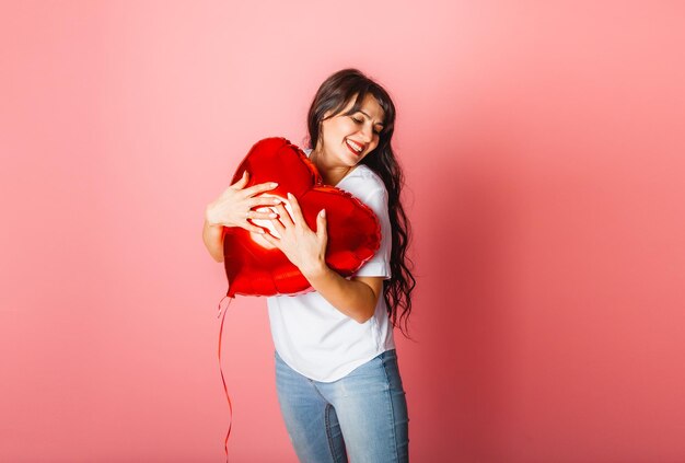 Glimlachend tevreden Kaukasisch meisje poseren met een rode hartvormige ballon op een roze achtergrond. Valentijnsdag