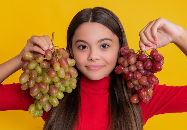 Glimlachend tienermeisje houdt tros druiven op gele achtergrond