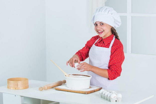 Glimlachend tienermeisje in chef-kok uniform koken en bakken van voedsel