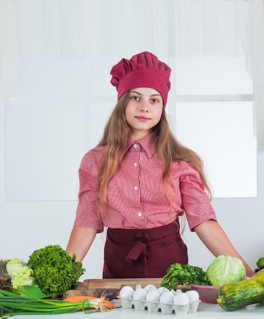 Glimlachend tienermeisje in chef-kok uniform koken groenten vegetarisch