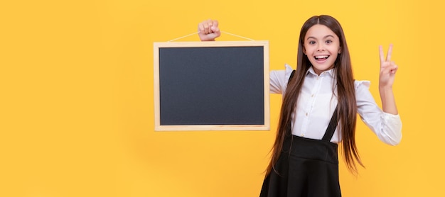 Glimlachend tienermeisje in uniform houdt schoolbord voor kopieerruimte met vredesschoolverkoop Banner van schoolmeisje student Schoolmeisje leerling portret met kopieerruimte