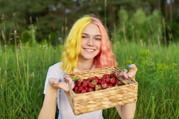 Glimlachend tienermeisje met aardbeien in de natuurachtergrond van de mandtuin