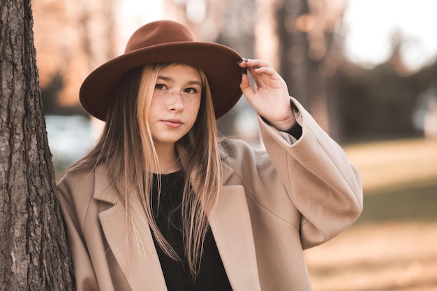 Glimlachend tienermeisje met stijlvolle hoed en beige winterjas