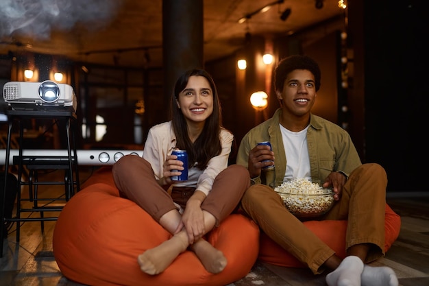 Glimlachend verliefde paar of vrienden kijken naar film thuis. Man en vrouw die frisdrank drinken en popcorn eten