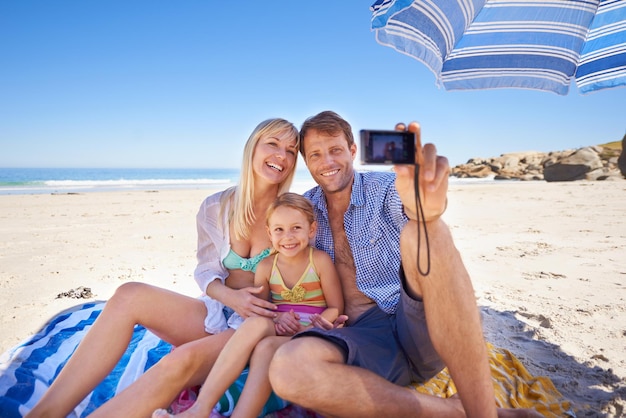 Glimlachend voor een vakantiefoto Shot van een gelukkig jong gezin dat een foto van zichzelf maakt op het strand