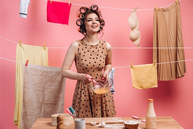 Glimlachend, vrolijk meisje in een bolletjestrui, eieren slaan, koken op de achtergrond van een touw met kleren.