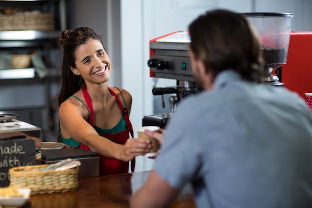 Foto glimlachend vrouwelijk personeel kopje koffie serveren aan een klant aan balie in winkel