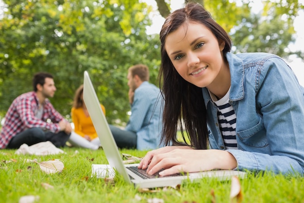 Glimlachend wijfje die laptop met andere studenten in park met behulp van